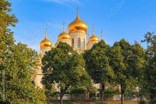 Cathedral of the Annunciation on Moscow Kremlin territory against blue sky and green trees in sunny early morning