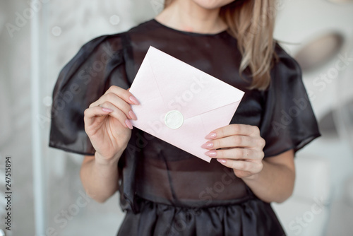 close-up photo of a female hands holding a pink invitation envelope with a wax seal, a gift certificate, a card, a wedding invitation card