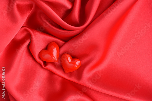 Two glass hearts on red satin fabric background