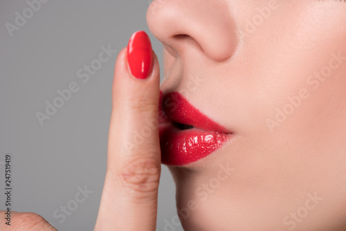 Beautiful girl holds finger with a manicure at plump lips with lipstick