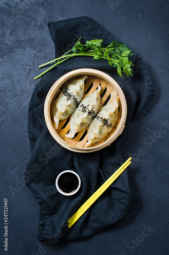 Japanese gyoza in a traditional steamer, yellow chopsticks. Dark background, top view