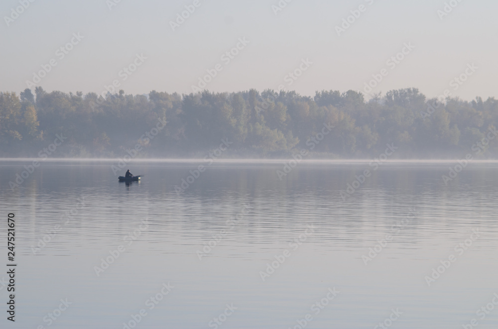 A fisherman on a boat catches fish at dawn in the middle of the river.