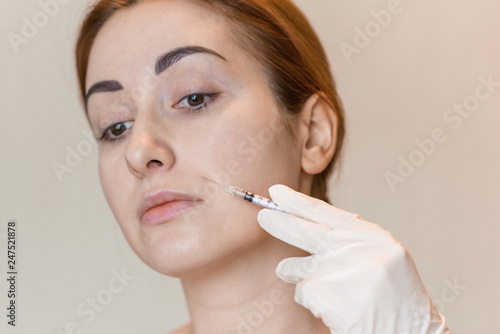 Natural look of young woman gets cosmetic injection. Doctors hands making an injection in face. Beauty Treatment 
