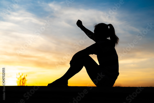 The silhouette of a woman sitting, feeling happy and raising her hand.