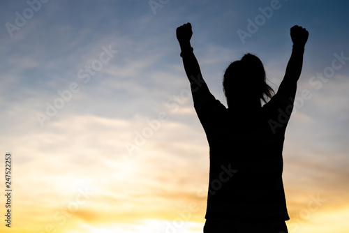 A happy young woman looks up at success and at sunset.