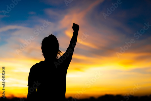 A happy young woman looks up at success and at sunset.