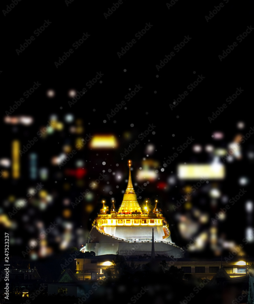 Wat Saket, Golden Mount temple on dark night, with blurred light bokeh of city.