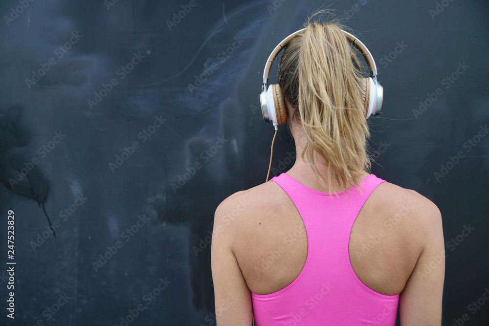 Back of strong toned woman in sportswear and headphones on black background