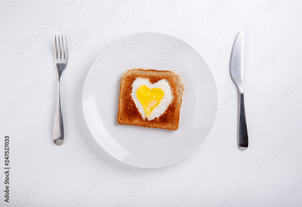 Toasted bread with fried eggs within on white plate. Heart Eggs. Festive breakfast on white table. Happy Valentines day. Top view. Copy space. Toasted bread with fried eggs within on white plate. Heart Eggs. Festive breakfast on white table. Happy Valentines day. Top view. Copy space.