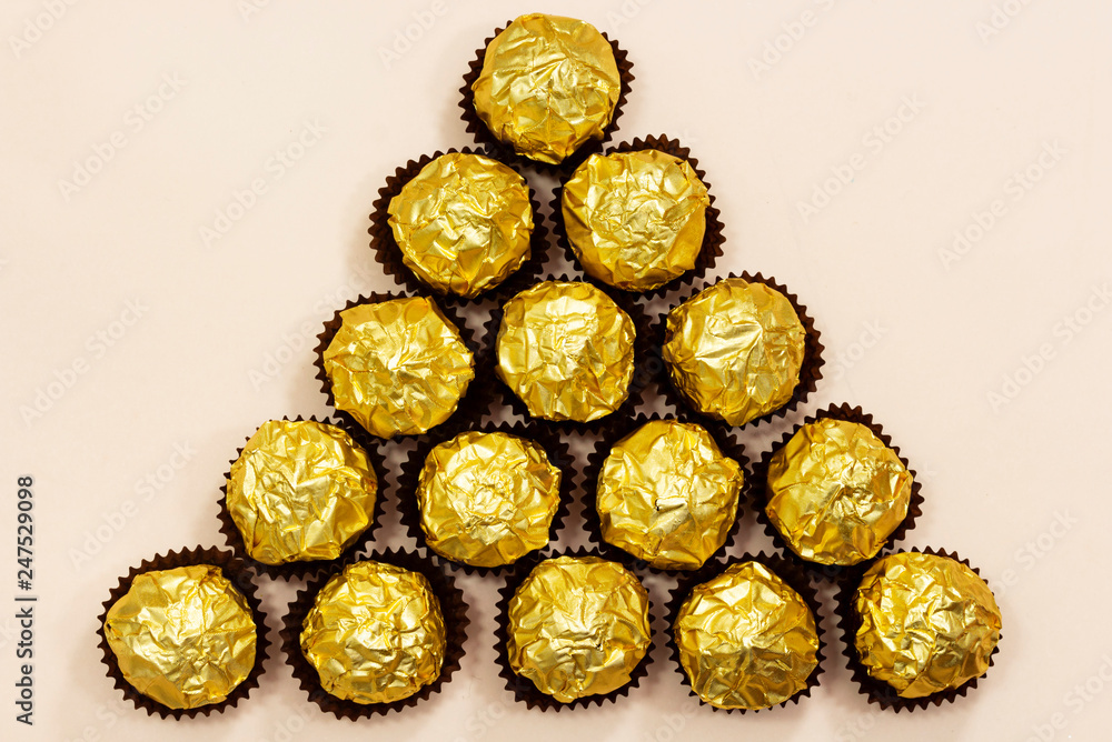forming triangle shape from golden premium chocolate sweets isolated on pink background forming triangle shape from golden premium chocolate sweets isolated on pink background