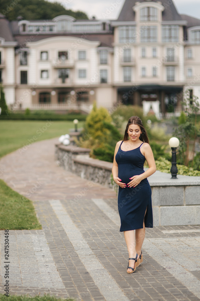 Pregnant woman in dress holds hands on belly