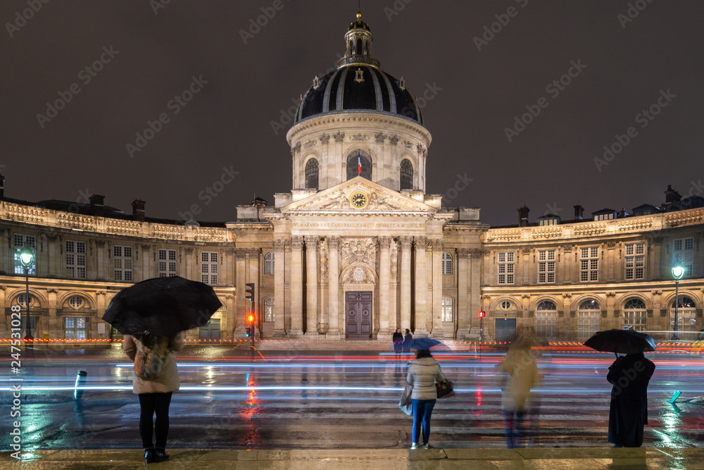 Obraz premium Paris, Institut de France during a rainy night. Tourists with umbrella and trails of light