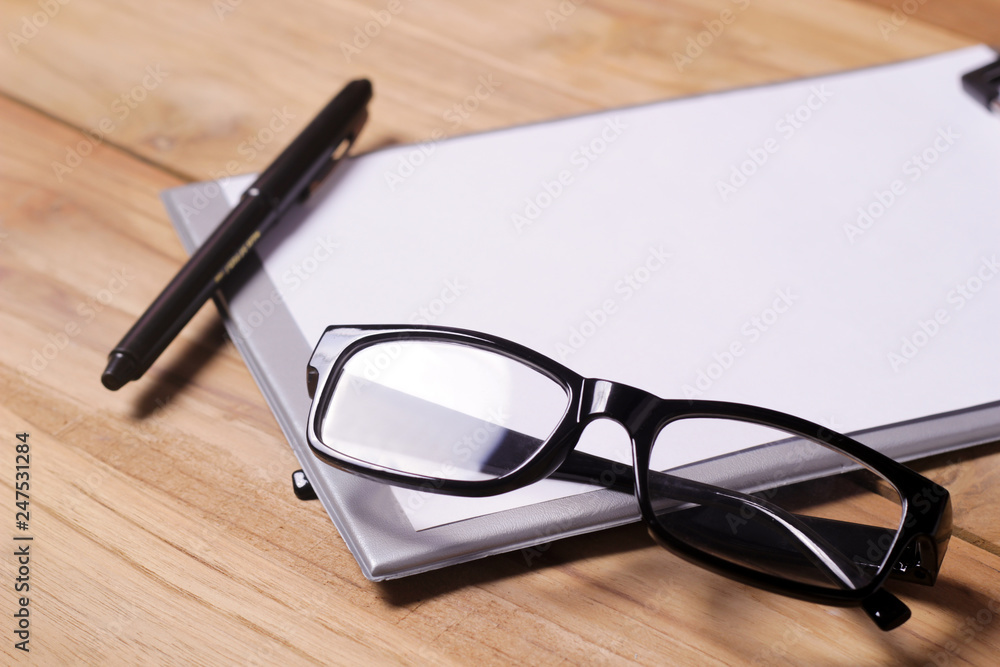 Working place on wooden table. Office desk table with eye glasses , shot notepaper pen,and smartphone. Working place on wooden table. Office desk table with eye glasses , shot notepaper pen,and smartphone.