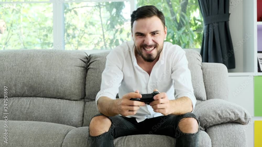 Young man playing console game in front of camera, beating his opponent online. White man on sofa. E-sport competition concept. Young man playing console game in front of camera, beating his opponent online. White man on sofa. E-sport competition concept.