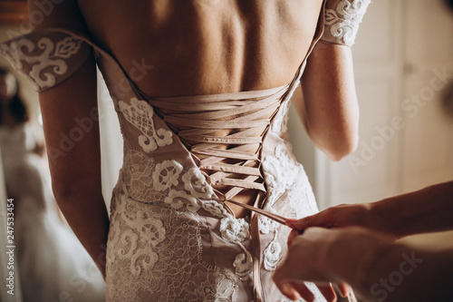 on the girl's white wedding dress, the bridesmaid tightens the ribbon on the corset of the dress photo