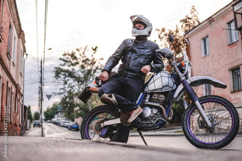 Fototapeta Naklejka Na Ścianę i Meble -  Handsome rider guy in helmet with off road enduro motorcycle at day time. Brutal urban lifestyle
