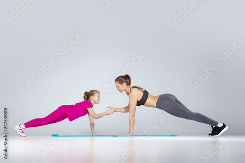 Beautiful woman and her little daughter are push ups at the gym