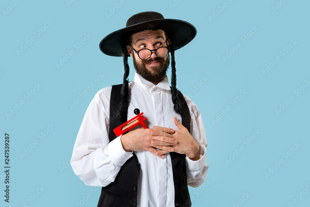 Portrait of a young orthodox Hasdim Jewish man with wooden Grager Ratchet at Jewish festival of Purim at studio. The purim, jewish, festival, holiday, celebration, judaism, pastry, tradition, cookie Portrait of a young orthodox Hasdim Jewish man with wooden Grager Ratchet at Jewish festival of Purim at studio. The purim, jewish, festival, holiday, celebration, judaism, pastry, tradition, cookie