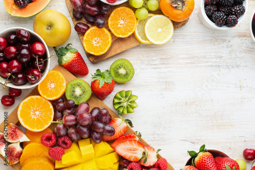 Healthy raw fruits background, cut mango, strawberries raspberries oranges plums apples kiwis grapes blueberries cherries, on white table, copy space, top view, selective focus