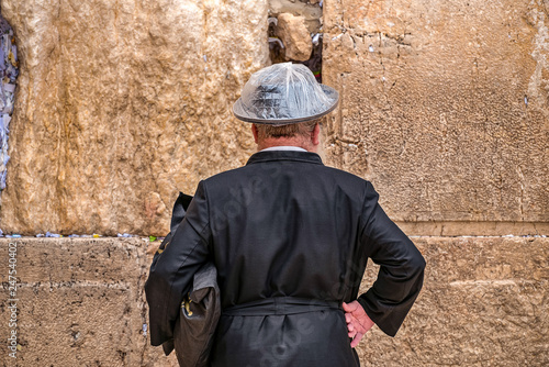 Believing Jew is praying near the wall of crying in a big black hat in a raincover under the rain photo