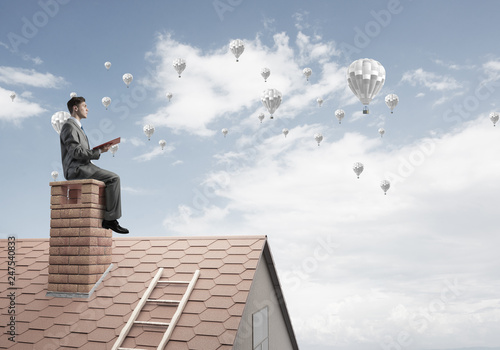 Man on roof reading book and aerostats flying in air