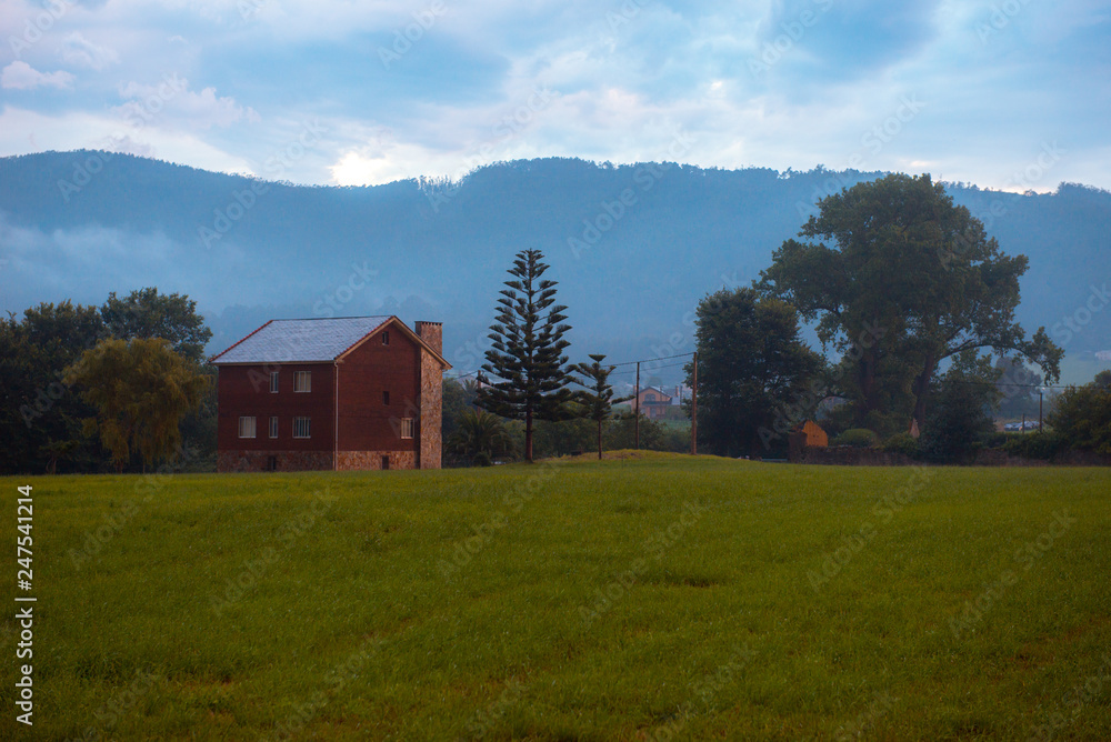 Wonderful view of field with fresh green grass and amazing brick house near spectacular hills on cloudy day in Ribadeo, Spain Wonderful view of field with fresh green grass and amazing brick house near spectacular hills on cloudy day in Ribadeo, Spain