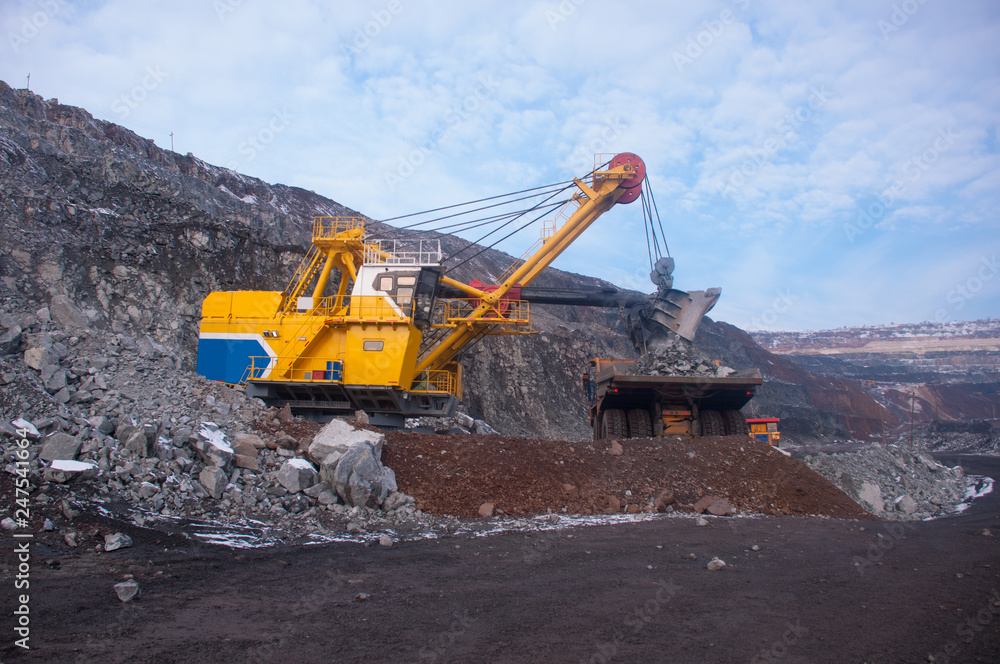 Excavator in the quarry loads the dumper with iron ore. Loading in winter Excavator in the quarry loads the dumper with iron ore. Loading in winter