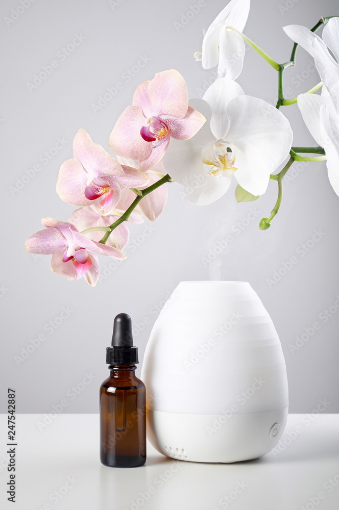 Oil diffuser with glass amber bottle and orchid flowers on white table