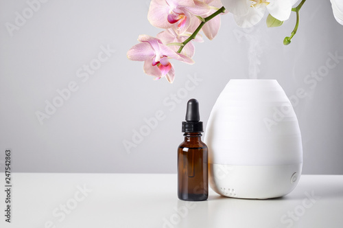 Obraz na płótnie Oil diffuser with glass amber bottle and orchid flowers on white table w salonie