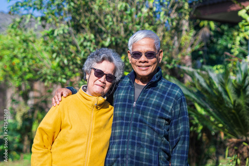 Portrait of elderly couple wearing sunglasses standing and smiling in home garden.