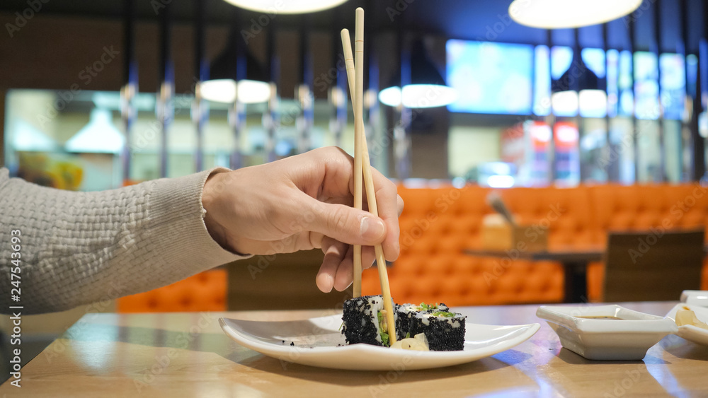 Young guy with chopsticks takes sushi from a plate in a japanese restaurant. Men starts eats japanese food.