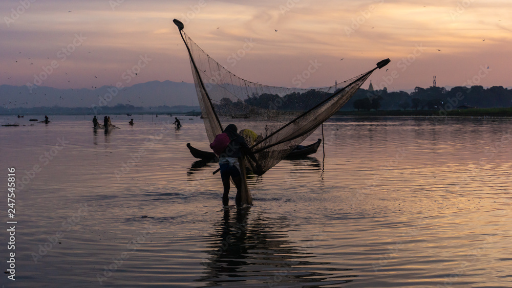 men fishing with triangular scoop net early morning at sunrise near iconic U-Bein Bridge, on shallow Lake Taungthamanin, Amarapura, Mandalay, Myanmar