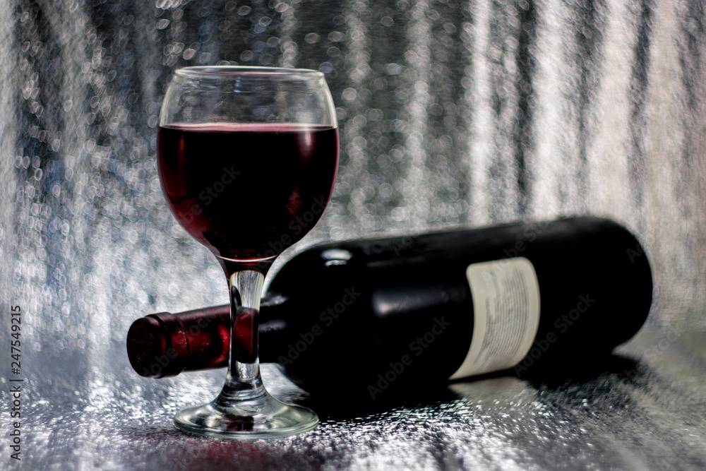 Fototapeta premium A glass of red grape wine, a bottle of wine on a silvery blurred bokeh background