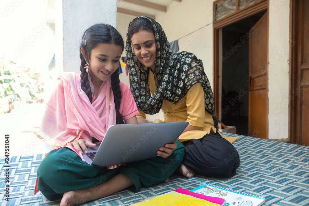 Happy village girl sitting with her mother on a cot at home operating a laptop computer. Happy village girl sitting with her mother on a cot at home operating a laptop computer.