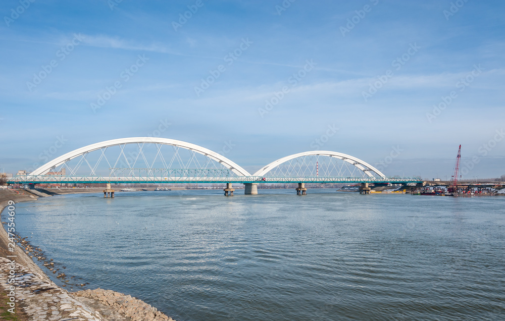 Naklejka premium New Serbian bridge with arc over the Danube river with architectural lines and blue sky above in city Novi Sad, Serbia