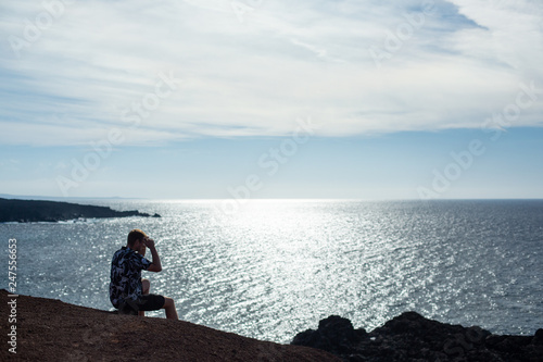 A man looks at the sea, sitting on a stone.