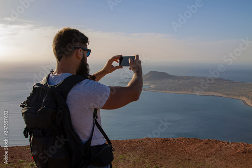 The man photographs an island in the ocean, standing on the edge of a cliff.