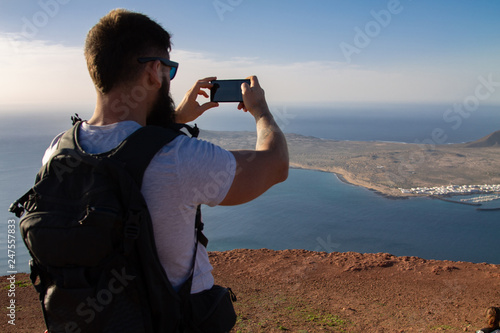 The man photographs an island in the ocean, standing on the edge of a cliff.