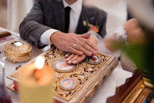 Newlyweds of groom and bride hold their hands on the golden Holy Bible while standing on the knees.