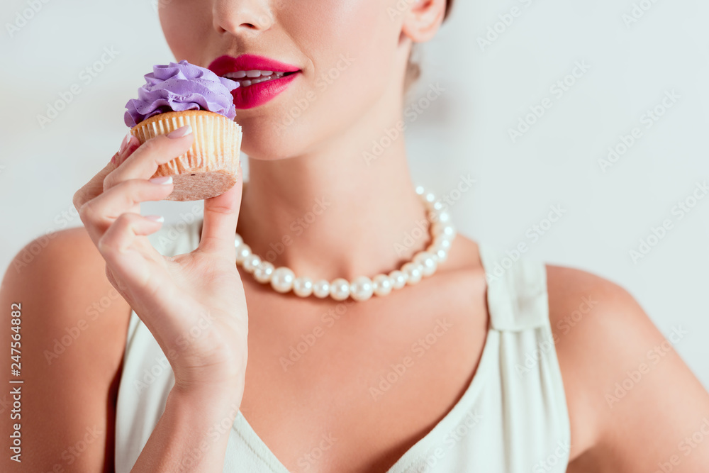partial view of pin up girl tasting homemade cupcake with purple cream