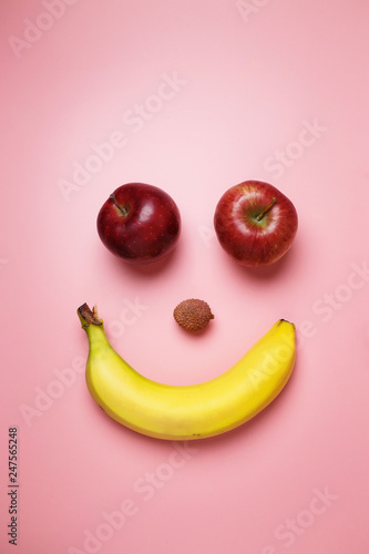 Smiley face with two apples and a banana with copy space on a pink background