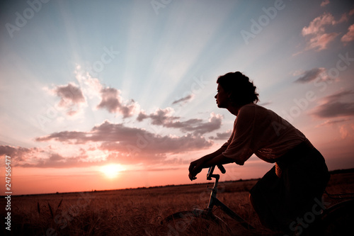 Silhouette of the girl behind the wheel of a bicycle on the background of a sunset in the clouds