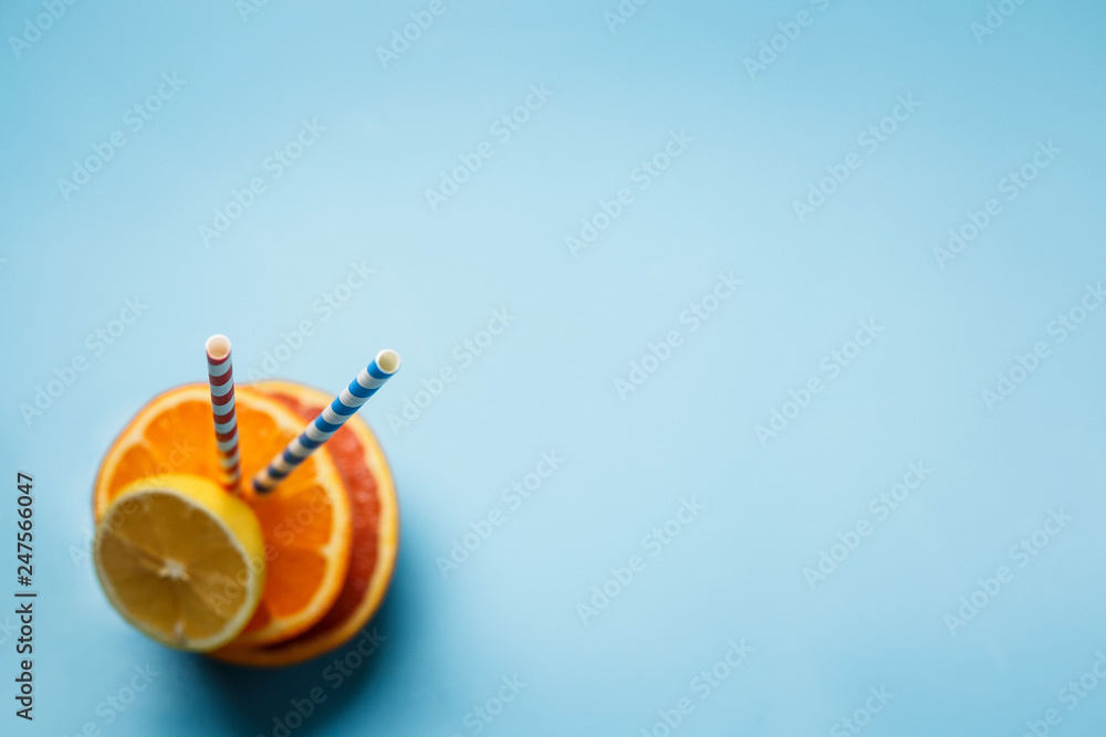 a glass of fresh juce and two paper tubes next to a lemon and an orange on a blue background with copy space a glass of fresh juce and two paper tubes next to a lemon and an orange on a blue background with copy space