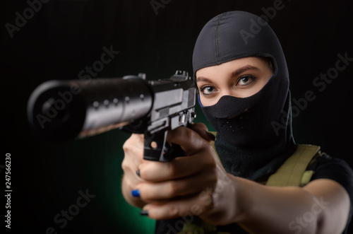Bild auf Leinwand the girl in military special clothes posing with a gun in his hands on a dark ba