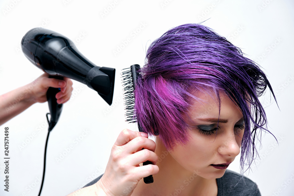 A girl in a gray t-shirt and makeup sitting with wet, purple and short hair on a white background in the middle of the frame. A girl in a gray t-shirt and makeup sitting with wet, purple and short hair on a white background in the middle of the frame.