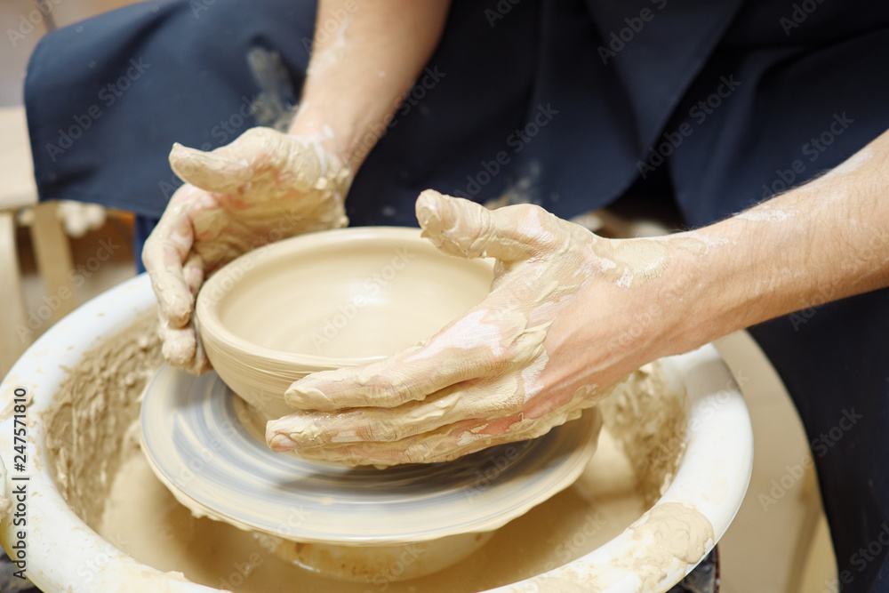 Woman man her hands dub wall jug, sculpts out of clay on circle. Dirty hands in the clay.