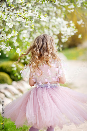 Beautiful young girl in pink dress in the garden with blosoming cherry trees. Cute girl having fun and enjoying