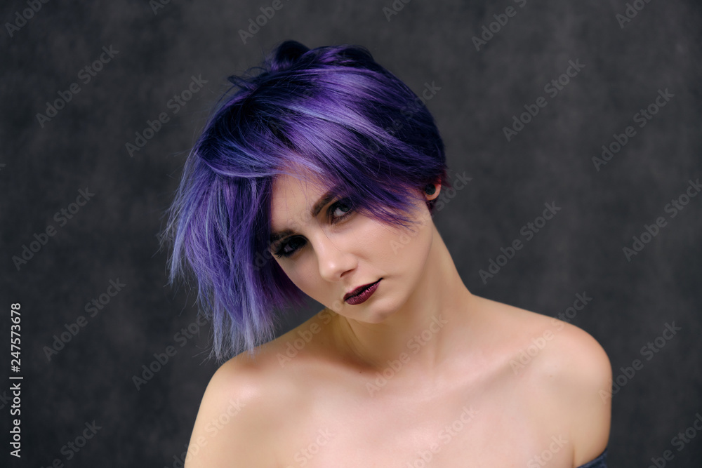 A beautiful, sexy girl with purple hair and a short haircut sits in the middle of the photo with a gray background A beautiful, sexy girl with purple hair and a short haircut sits in the middle of the photo with a gray background