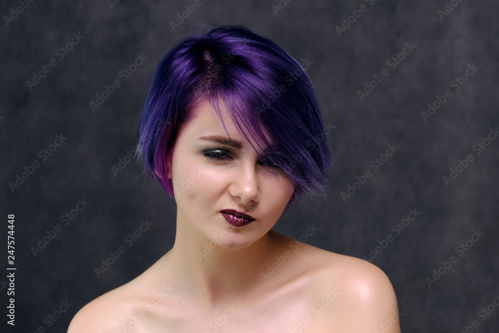 A beautiful, sexy girl with purple hair and a short haircut sits in the middle of the photo with a gray background A beautiful, sexy girl with purple hair and a short haircut sits in the middle of the photo with a gray background