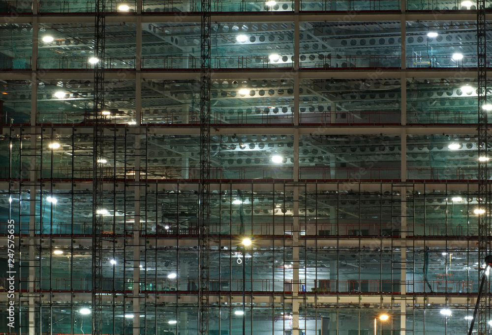 a full frame view of a large construction site at night illuminated by bright work lights with girders and construction hoists